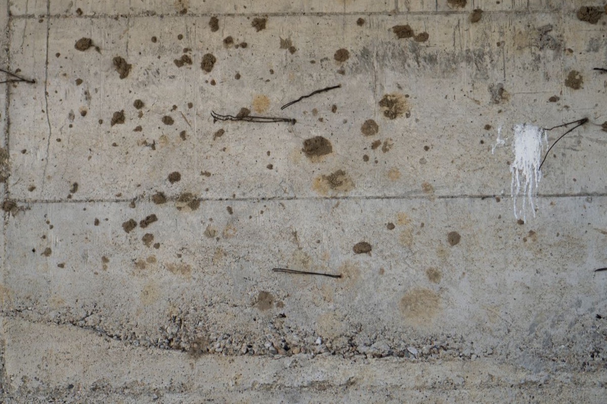 Weathered reinforced-concrete wall with exposed rusting tie-wires and spalling